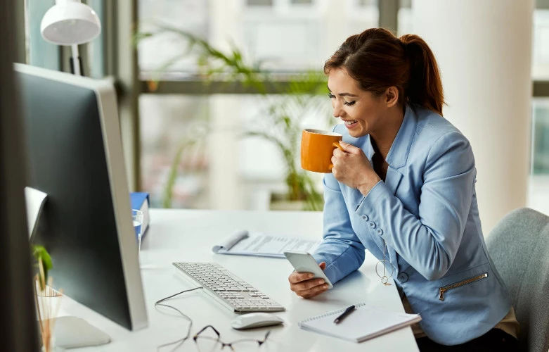 Happy female employee drinking tea in front of the computer